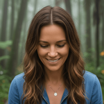 Woman in a blue jacket standing in a forest with a dog.